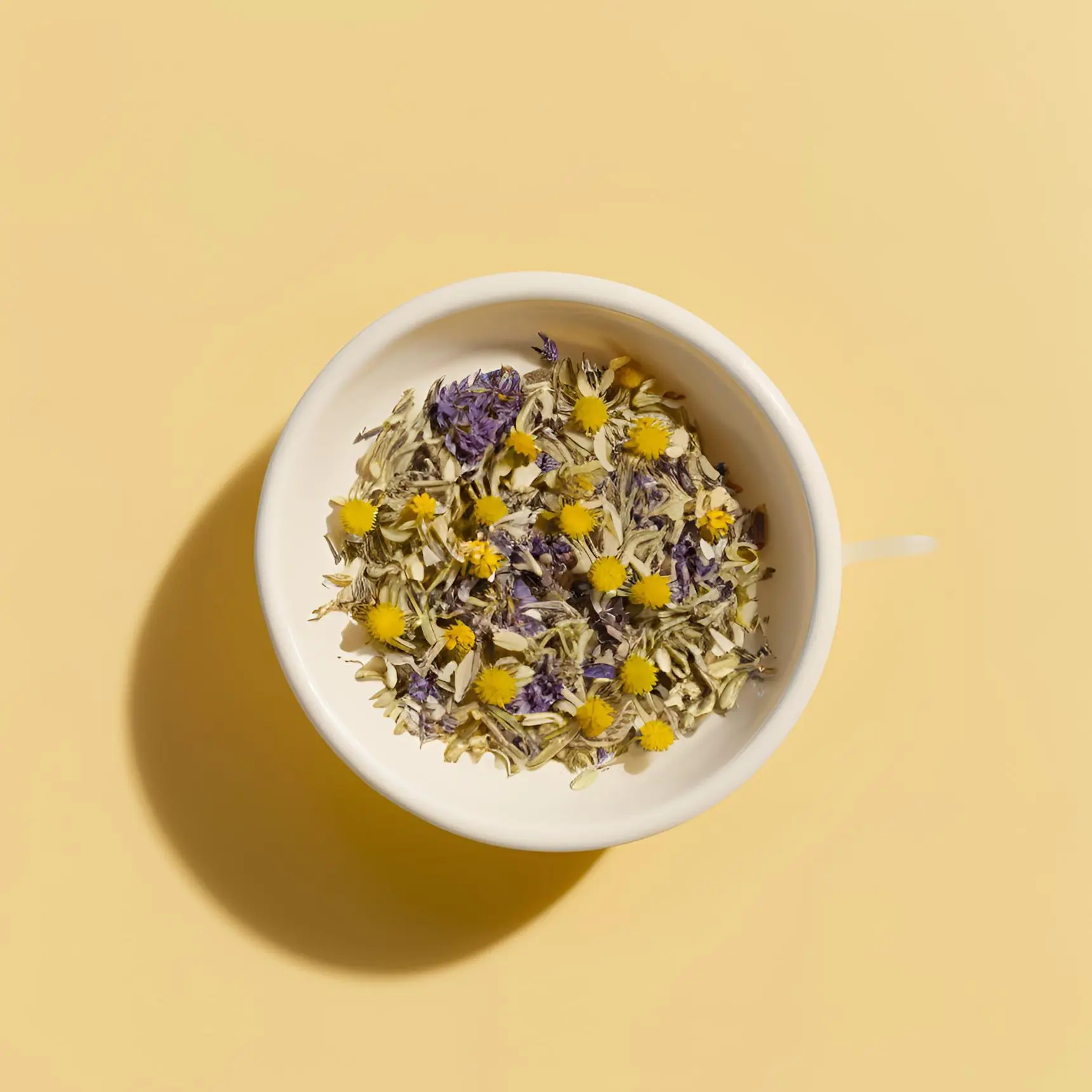 A bowl of dried chamomile flowers and cornflower petals, the botanicals used in Moody Teas herbal blends